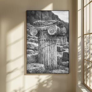 Puede incluir: Fotografía en blanco y negro de una columna jónica clásica, que muestra intrincados adornos en espiral en el capitel. La columna de piedra desgastada se alza entre ruinas antiguas, con un telón de fondo montañoso, evocando historia y arquitectura.