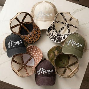 May include: A collection of trucker hats in various colors and patterns, including leopard print, camouflage, and solid colors. Each hat features the word "Mama" embroidered in a cursive font. The hats have mesh backs and curved brims.