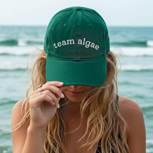 May include: A dark green baseball cap featuring the text team algae embroidered in white thread across the front panel. The cap has a structured crown, a curved brim, and a button on top, providing a classic look for casual outdoor wear.