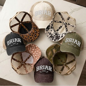 May include: A collection of trucker hats in various colors and patterns. The hats feature the word "BRIAR" in white block letters with crossed hockey sticks. Designs include solid colors, animal prints, and camouflage, with mesh backs and curved brims.