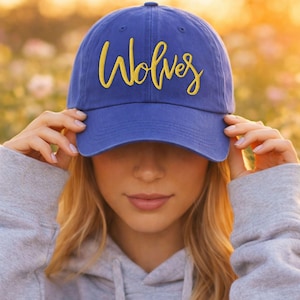 Peut inclure: Une casquette de baseball bleu roi avec le mot Wolves brodé en écriture cursive jaune sur le panneau avant. La casquette présente une calotte structurée, une visière incurvée et un bouton sur le dessus, offrant un contraste de couleurs vif.