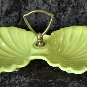 May include: A light green, two-section serving dish with a gold-colored handle. The dish has a scalloped edge and a shell-like design. The handle is attached to a central, decorative post.