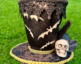 Black off white bat top Hat. Embellished with skull , black and gold trim. Flexible brim Perfect for a pumpkin, skeleton wreath or Halloween