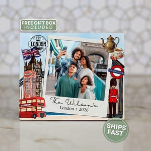 May include: A decorative photo frame featuring a family photo in front of the Tower Bridge in London. The frame includes illustrations of a red double-decker bus, a British flag, and a London Underground sign. Text reads "The Wilson's London 2026."