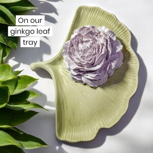 A muted pink fragrance stone that has essential oils added to it to fragrance the air. It is sitting on a green ginkgo Leaf shaped tray and is next to some green plants and a cottage core living room