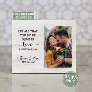 May include: A rectangular wooden photo plaque with a white wood grain finish. The left side features the text "LET ALL THAT YOU DO BE DONE IN LOVE 1 CORINTHIANS 16:14" above the names "Oliver & Kari" and the date "MAY 30, 2026". A photo is on the right.