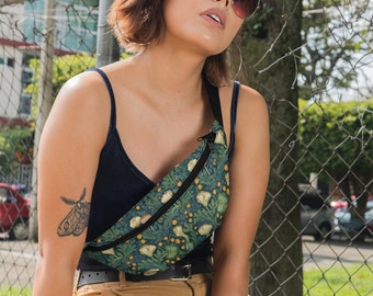 May include: A woman wearing a black tank top and brown pants is wearing a green and yellow fanny pack with a floral pattern. The fanny pack has a zipper closure and a black strap.
