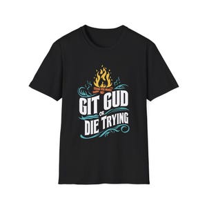Puede incluir: Camiseta negra con un diseño gráfico azul y naranja. El gráfico presenta una fogata con llamas y el texto "Git Gud or Die Trying."