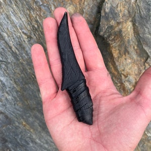 Può includere: Un coltello in legno nero intagliato a mano con una lama curva e un manico testurizzato.