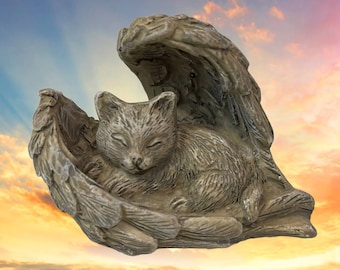 May include: A stone-colored cat figurine resting peacefully within a pair of textured angel wings. The cat is curled up with its eyes closed, and the wings have a detailed feather design. The sculpture is set against a colorful sky background.