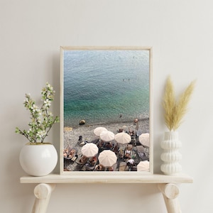 Peut inclure: Vue a&eacute;rienne d'une plage avec des parasols blancs et des personnes se relaxant sur des chaises longues. L'eau est d'un bleu turquoise vibrant et le sable est d'un beige clair.