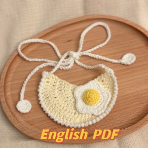 May include: A crocheted bib with a white egg design. The bib is yellow and has a white border. The bib is tied with white strings. The text "English PDF" is visible at the bottom of the image.
