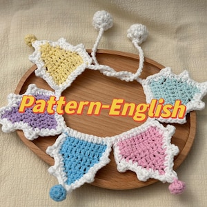 Puede incluir: Una guirnalda de crochet con cinco banderas triangulares de colores. Las banderas son moradas, amarillas, azules, rosas y azules. La guirnalda está enhebrada en un cordón blanco con pompones blancos en cada extremo.