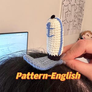 以下が含まれることがあります： 錨のデザインが施された、青と白のクロシェのセーラーハットヘアクリップ。Pattern-English.