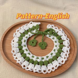 May include: A white and green crocheted collar with a bow. The collar is made with a delicate stitch pattern and features a row of green circles.