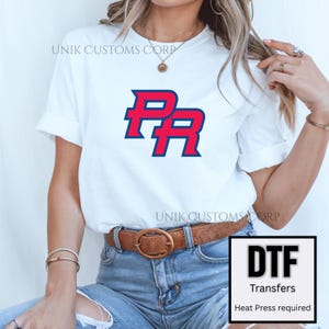 Pode incluir: Camiseta branca com o logotipo "PR" vermelho e azul. A camiseta é combinada com jeans azuis e um cinto marrom. A imagem inclui um gráfico "DTF Transfers", indicando transferências de prensa térmica.