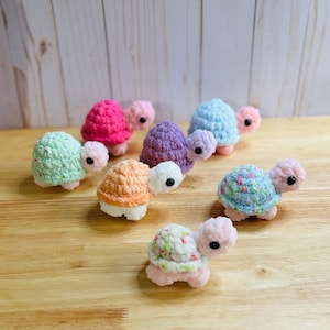 May include: A collection of seven crocheted turtle toys in various colors, including pink, green, purple, orange, and blue. The turtles have small, black eyes and are made with a textured yarn.