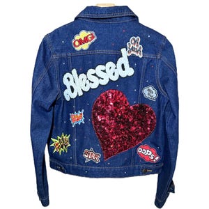 May include: A blue denim jacket with various colorful patches, including a large red sequined heart, and the word "Blessed" in white lettering.