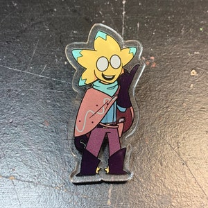 Op de afbeelding: Een geel, stervormig personage met een blauwe cape en een paarse broek. Het personage draagt een bril en heeft een brede glimlach. Het personage houdt een pistool in zijn rechterhand en zwaait met zijn linkerhand. Het personage is een cartoonachtige illustratie.