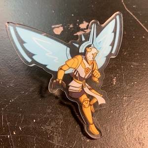 May include: A clear acrylic keychain featuring a cartoon illustration of a winged knight in gold armor, holding a sword and shield. The knight has a white helmet with a cross on it and is running forward. The wings are blue and white.