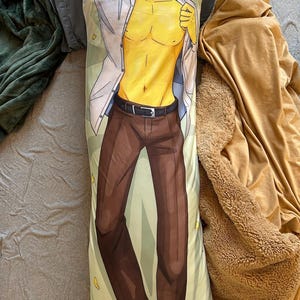 May include: A rectangular body pillowcase featuring a printed illustration of a yellow-skinned character with spiky blonde hair, wearing an unbuttoned white shirt, dark brown trousers with a black belt, and black shoes against a light green background.