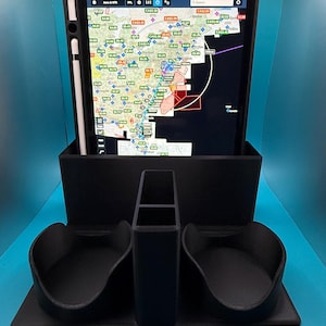 May include: A black 3D-printed tablet holder with a built-in stand and storage compartments. The tablet displays a detailed map with various markers and data. A stylus is placed on the side of the tablet. The holder is on a blue surface.