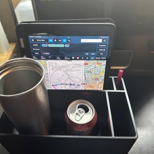 May include: A black organizer with multiple compartments, holding a silver travel mug, a can of soda, and a tablet displaying a map and flight information.