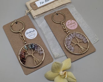 May include: Two gold wire wrapped tree of life keychains with different colored gemstones. The keychain on the left has red, orange, yellow, green, blue, and purple gemstones. The keychain on the right has pink gemstones. Both keychains have a small round tag that says "Handmade with love".