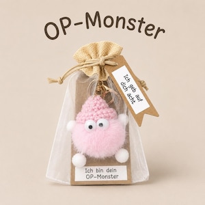 Könnte beinhalten: Ein flauschiger rosa Monster-Schlüsselanhänger mit gehäkelter Mütze und Wackelaugen in einem transparenten Beutel. Ein braunes Etikett am Beutel trägt die Aufschrift Ich geb auf dich acht und ein Schild vorne zeigt Ich bin dein OP-Monster.