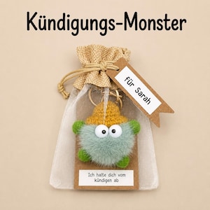 Könnte beinhalten: Ein flauschiger hellgrüner Monster-Schlüsselanhänger mit gelbem Hut und großen weißen Augen, verpackt in einem Organzabeutel. Ein braunes Etikett am Beutel trägt den Text 'für Sarah' und 'Ich halte dich vom kündigen ab'.