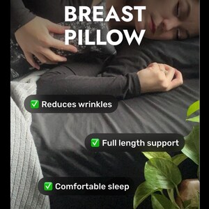 Może przedstawiać: Ciemnoszara poduszka na biust we wzory z białym napisem BREAST PILLOW, Reduces wrinkles, Full length support oraz Comfortable sleep. Poduszka jest trzymana przy klatce piersiowej na czarnej powierzchni z zielonymi liśćmi.