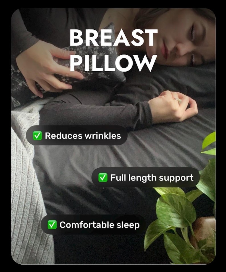 Może przedstawiać: Ciemnoszara poduszka na biust we wzory z białym napisem BREAST PILLOW, Reduces wrinkles, Full length support oraz Comfortable sleep. Poduszka jest trzymana przy klatce piersiowej na czarnej powierzchni z zielonymi liśćmi.