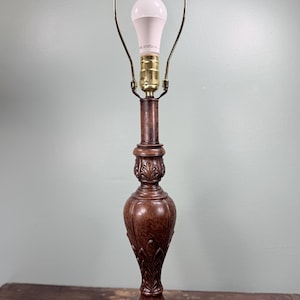 May include: A brown, ornate table lamp with a white bulb. The lamp has a detailed, carved base and a brass-colored neck and bulb holder. The lamp is approximately 20 inches tall.