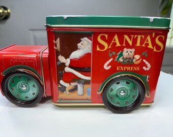 May include: A red and green metal Santa's Express truck-shaped tin. The tin features an illustration of Santa Claus and the words "SANTA'S EXPRESS". The wheels are green and the tin is rectangular.
