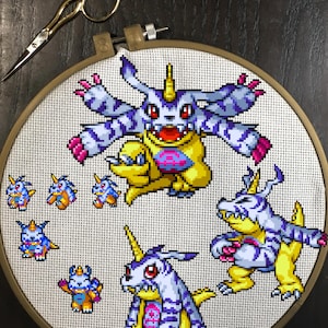 May include: Cross-stitch embroidery of a yellow and blue cartoon character with a horn on its head. The character is surrounded by smaller versions of itself in different poses.