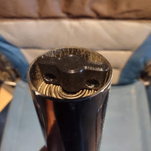 May include: Close-up of a black and silver bottle opener. The opener has a cylindrical shape with a black top and a silver interior. The top has a unique design with a small, raised section.