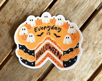 Könnte beinhalten: Ein Halloween-Aufkleber in Form eines Kuchenstücks. Der Kuchen hat einen orangen Zuckerguss, weiße Geister- und Kürbisdekorationen und den Text "Everyday is Halloween". Schwarze Fledermäuse sind ebenfalls enthalten.