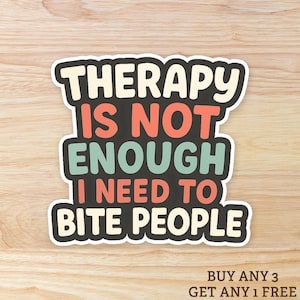 Può includere: Un adesivo con la scritta "THERAPY IS NOT ENOUGH I NEED TO BITE PEOPLE" in un carattere giocoso. L'adesivo ha un bordo nero ed è posto su uno sfondo di venature di legno chiaro. Il testo è in vari colori.