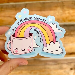 May include: A sticker with a light blue background featuring a pink mug with a smiling face, a rainbow, and white clouds. The text "you can't pour from an empty cup" is written around the rainbow.