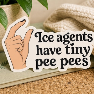 May include: A die-cut sticker with a cream background featuring a graphic illustration of a hand making a small gesture with fingers pinched together, accompanied by the black text "Ice agents have tiny pee pees" with a small heart above the letter i.