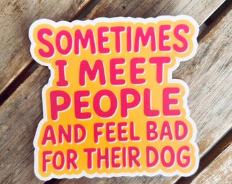 May include: A yellow sticker with the text "SOMETIMES I MEET PEOPLE AND FEEL BAD FOR THEIR DOG" in pink letters. The sticker has a white border and is on a wooden surface.