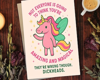 May include: A greeting card with a pink unicorn illustration. The card reads "NOT EVERYONE IS GOING TO THINK YOU'RE AMAZING AND MAGICAL. THEY'RE WRONG THOUGH. DICKHEADS." The unicorn has a yellow horn, pink mane, and green wings.