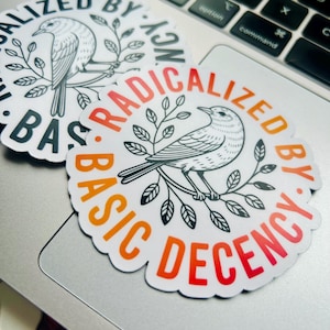 以下が含まれることがあります： ノートパソコンに、枝にとまった鳥が描かれた3つの白いステッカーが表示されています。ステッカーは、オレンジと赤で「RADICALIZED BY BASIC DECENCY」、黒で「BASIC DECENCY」と書かれた円形デザインです。