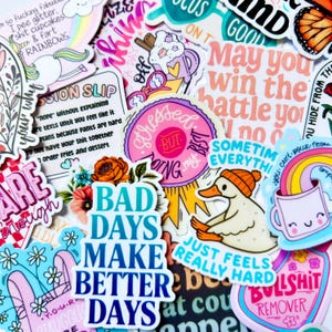 Puede incluir: Una colección de pegatinas coloridas con varios diseños y texto. Las pegatinas presentan frases como "Bad Days Make Better Days", "Stressed But Doing My Best" y "Just Feels Really Hard". Otros diseños incluyen un pato con sombrero, un arcoíris y un unicornio.