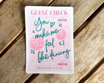 May include: A pink guest check sticker with the words "You make me feel like dancing" in green script. The sticker also features two disco ball graphics and the text "GUEST CHECK" at the top.