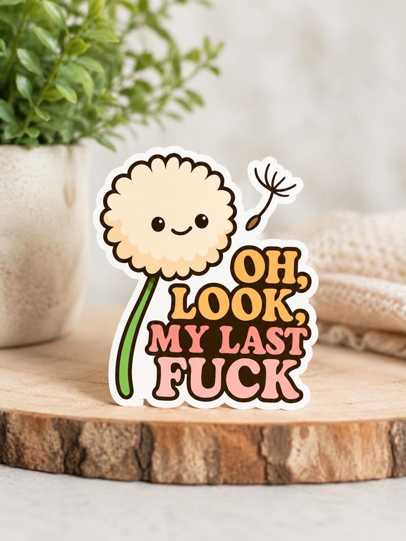Op de afbeelding: Een sticker met een cartoon paardenbloem met een lachend gezicht. De tekst "OH, LOOK, MY LAST FUCK" staat in oranje en roze. De sticker is geplaatst op een houten oppervlak.