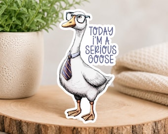 Może przedstawiać: Naklejka z białej gęsi w okularach i krawacie, z napisem "TODAY I'M A SERIOUS GOOSE". Gęś ma pomarańczowe stopy i żółty dziób. Naklejka znajduje się na drewnianej powierzchni.