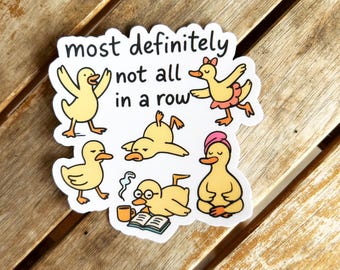Puede incluir: Una pegatina blanca con seis patos amarillos de dibujos animados en varias poses. La pegatina tiene el texto "most definitely not all in a row". Un pato está bailando, otro leyendo y otros están en posturas de yoga.