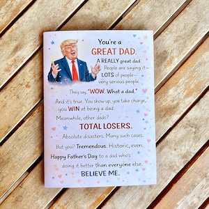 May include: A Father's Day greeting card with a picture of a man in a suit and tie. The card has text that reads "You're a GREAT DAD" and other phrases. The card is white with blue and pink star accents.
