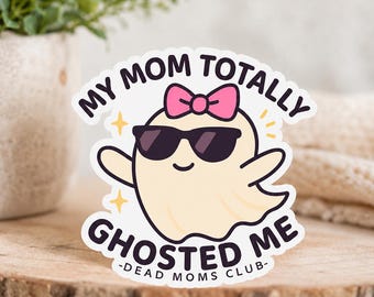 Könnte beinhalten: Ein gestanzter Aufkleber mit einem blassgelben Cartoon-Geist, der eine schwarze Sonnenbrille und eine rosa Schleife trägt. Der Text lautet MY MOM TOTALLY GHOSTED ME und -DEAD MOMS CLUB- in dunkelvioletter Schrift, ergänzt durch kleine gelbe Sterne.